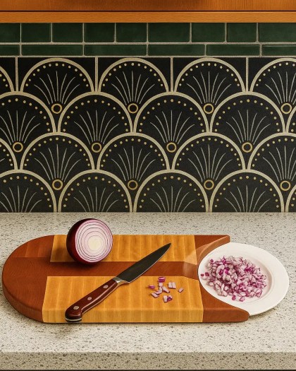 Sled cutting board handcrafted from Maple and Cherry wood, displayed on a kitchen countertop with a sliced red onion and knife beside a patterned backsplash