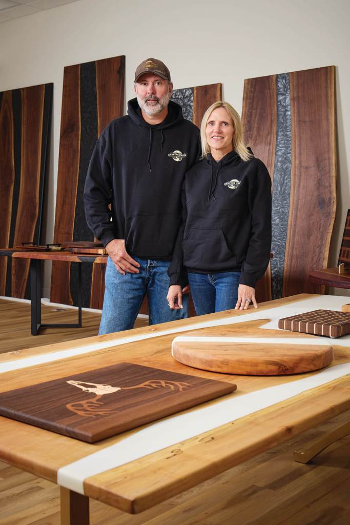 Ryan and Katie Rush standing in the Carvers Creek showroom surrounded by handcrafted live-edge walnut tables featured in Baltimore Magazine.