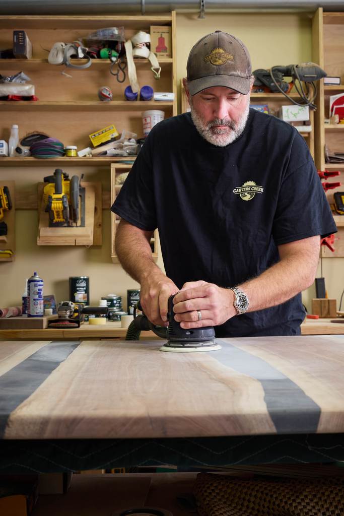 Ryan Rush sanding a live-edge walnut and resin table at the Carvers Creek workshop in Hunt Valley, Maryland — featured in Baltimore Magazine.